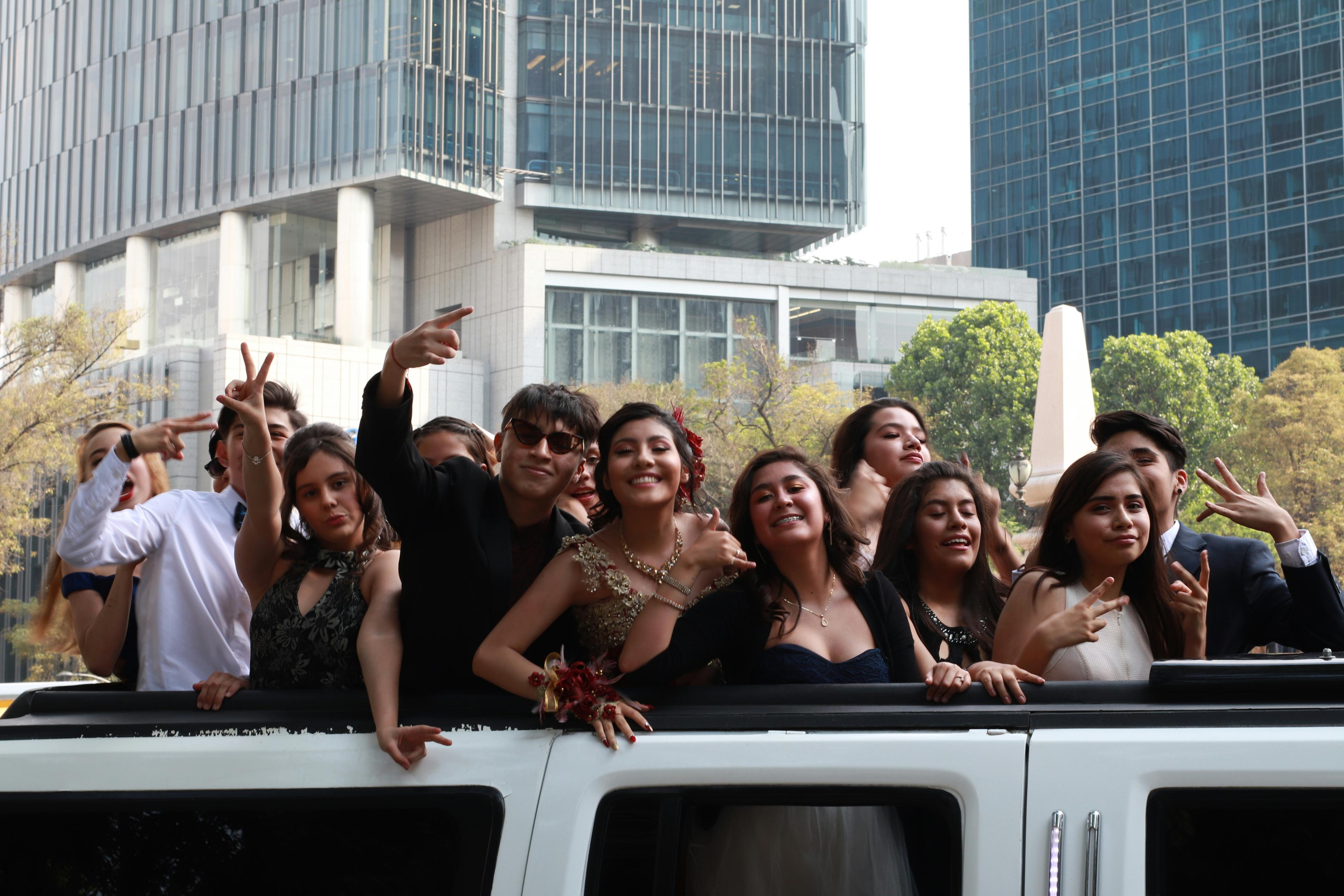 Teenagers in formal prom attire posing in front of a luxury stretch limousine for photos
